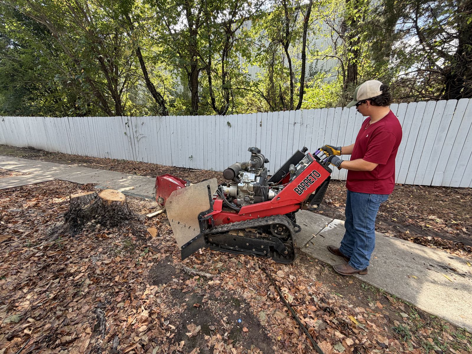 Carter running a walk-behind stump grinder beside a house in Northwest Arkansas